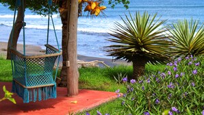 A hammock chair, a palm tree, and purple flowers by the beach. - Suite San Juan 135 Gran Pacifica Resort (Villa El Carmen)