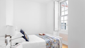 A minimalist bedroom with a bed, bedside table, lamp, and a window with a view of the outside. - Chiado | SPACIOUS & PEACEFUL | Family-Friendly (Lisboa)