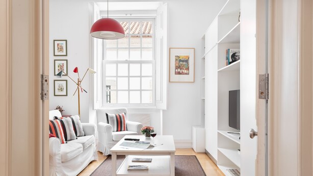 A modern living room with a white sofa, a coffee table, and a red pendant light. There are framed pictures on the wall and a bookshelf with a TV on top. - Chiado | SPACIOUS & PEACEFUL | Family-Friendly (Lisboa)