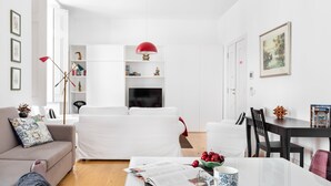 A modern living room with a white sofa, a dining table with a vase of flowers, and a bookshelf with decorative items. - Chiado | SPACIOUS & PEACEFUL | Family-Friendly (Lisboa)