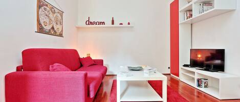 Un salon moderne avec un canapé rouge, une table basse blanche et un téléviseur posé sur un meuble blanc.