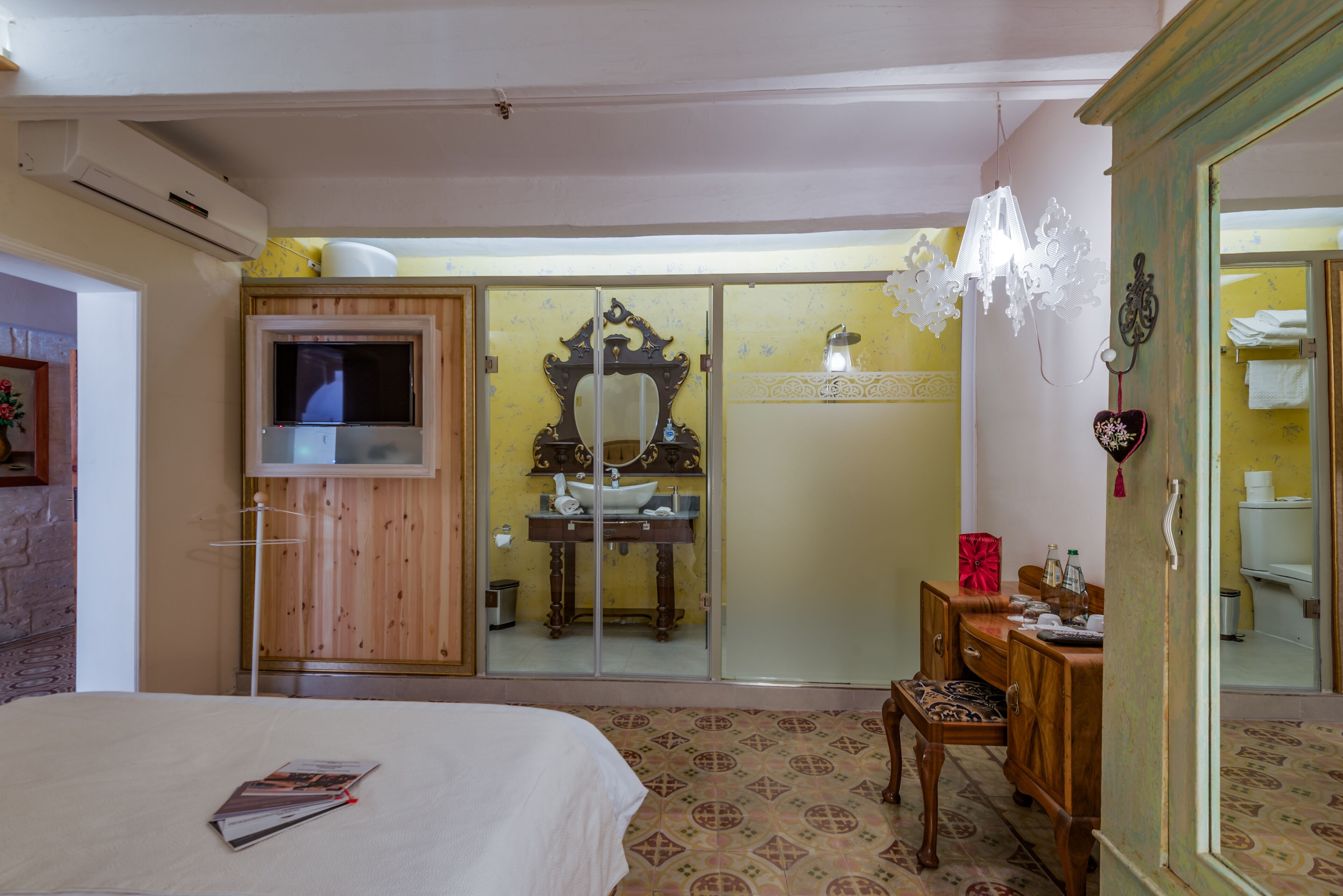 Ein Hotelzimmer mit einem Bett, einem Holzschrank, einem Schminktisch mit Spiegel, einem Fernseher und einem durch eine Schiebetür einsehbaren Badezimmer.