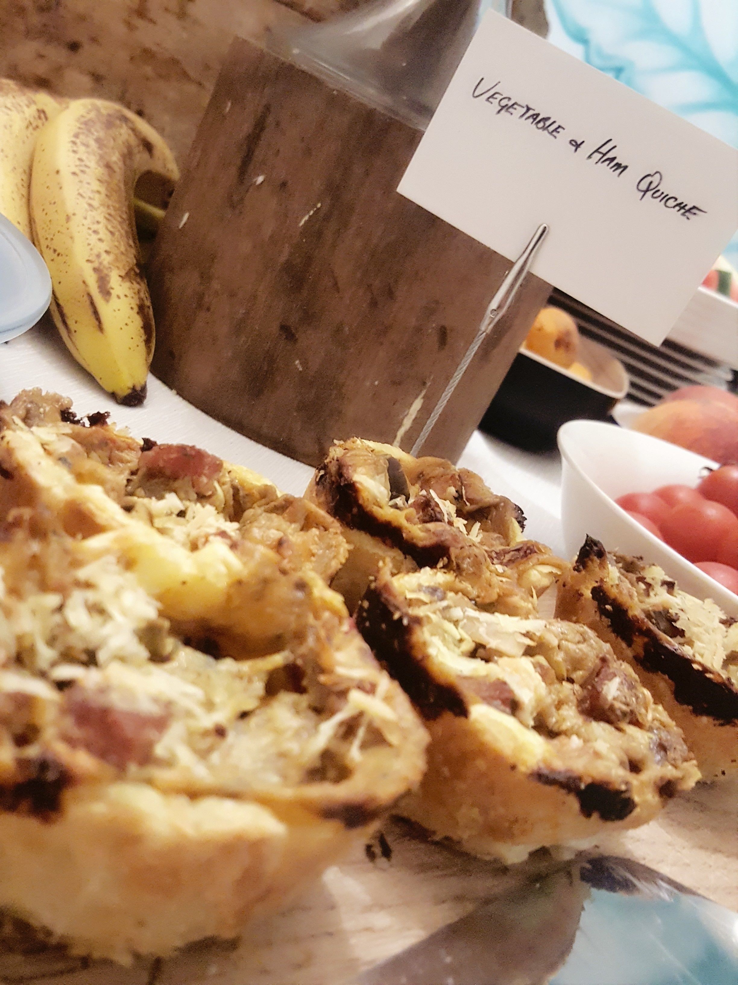 Um prato de sobremesas com uma placa que diz 'Quiche de Legumes e Presunto'.
