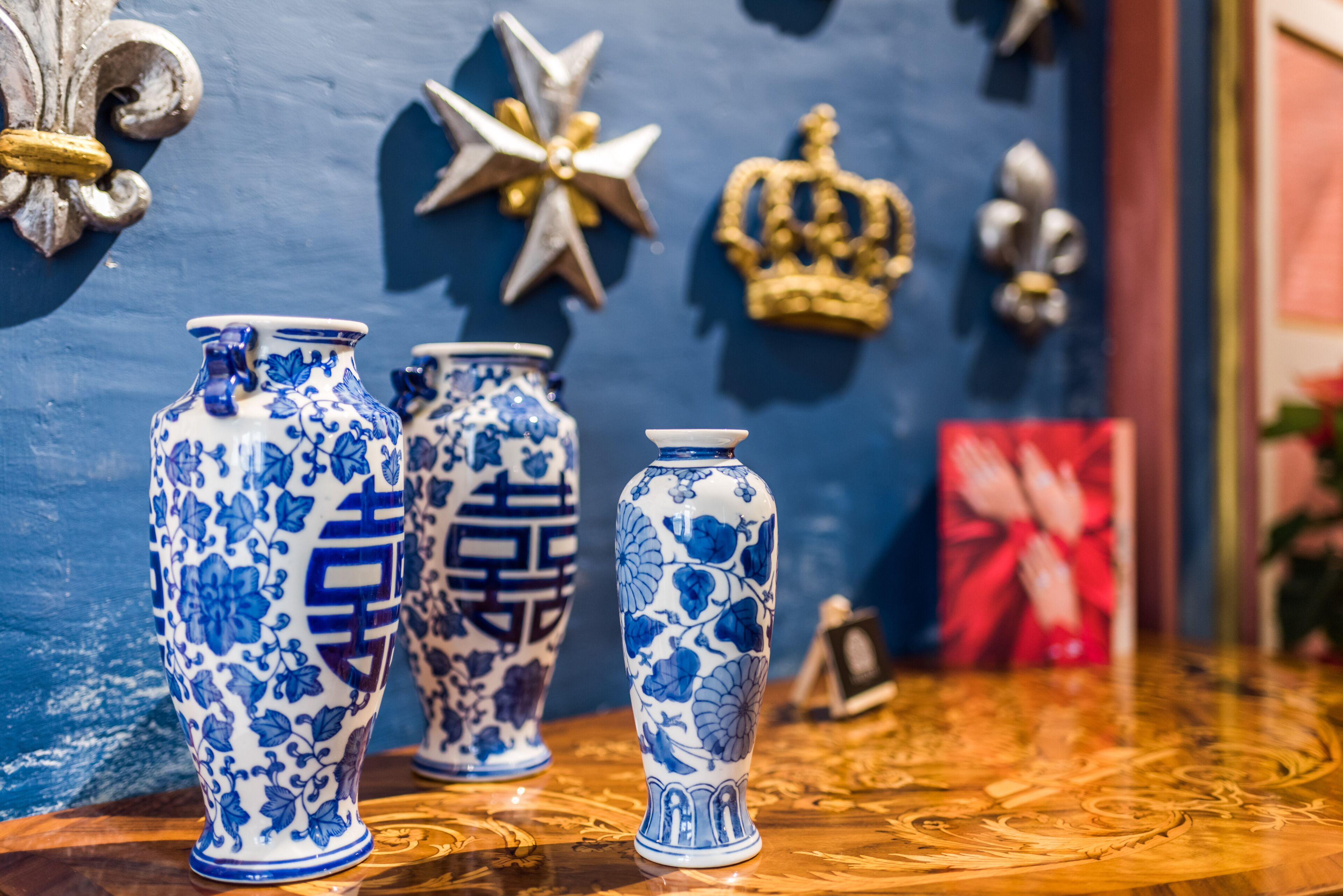Três vasos azuis e brancos com padrão sobre uma superfície de madeira, com elementos decorativos ao fundo.