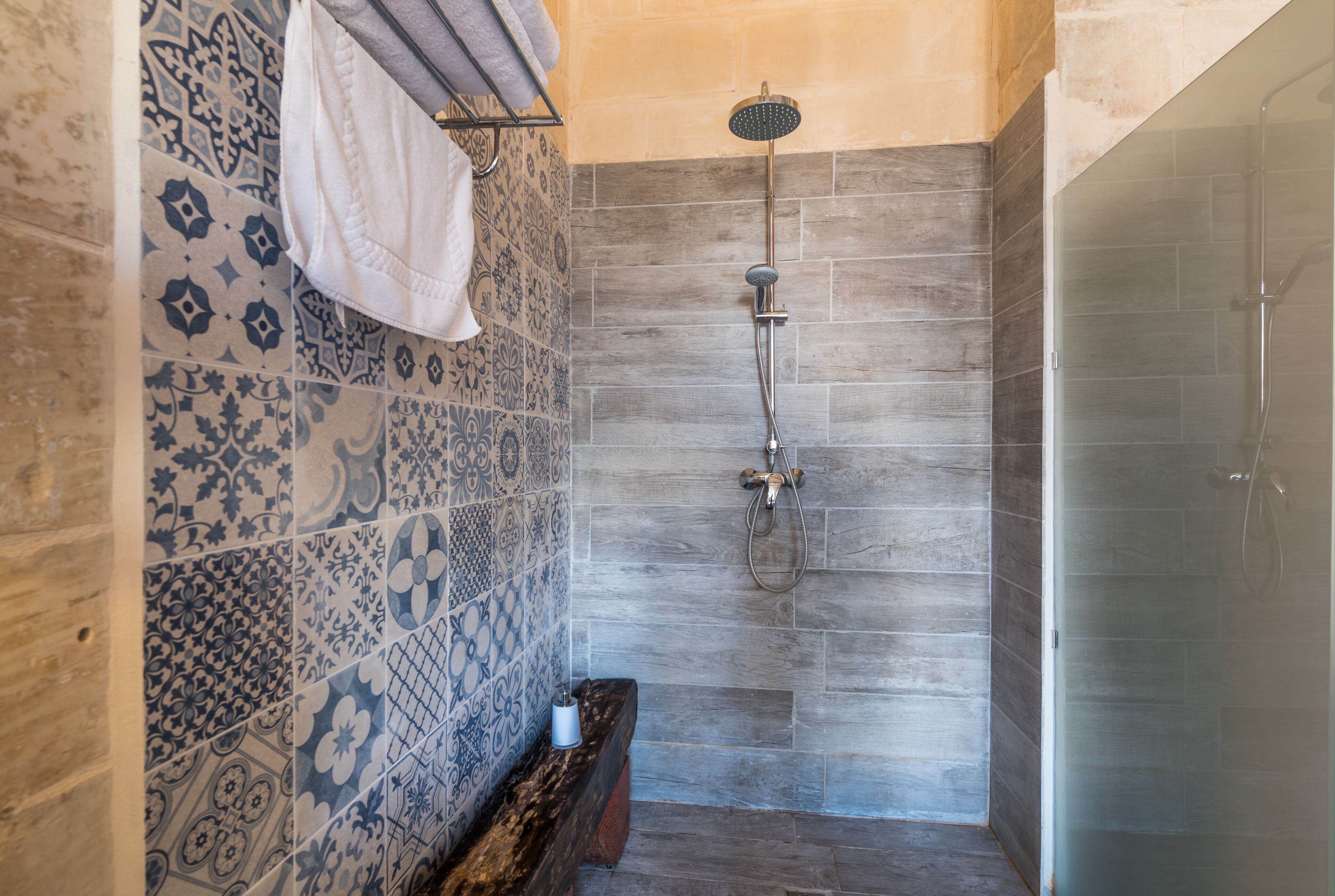 Un baño con baldosas estampadas, ducha y banco.