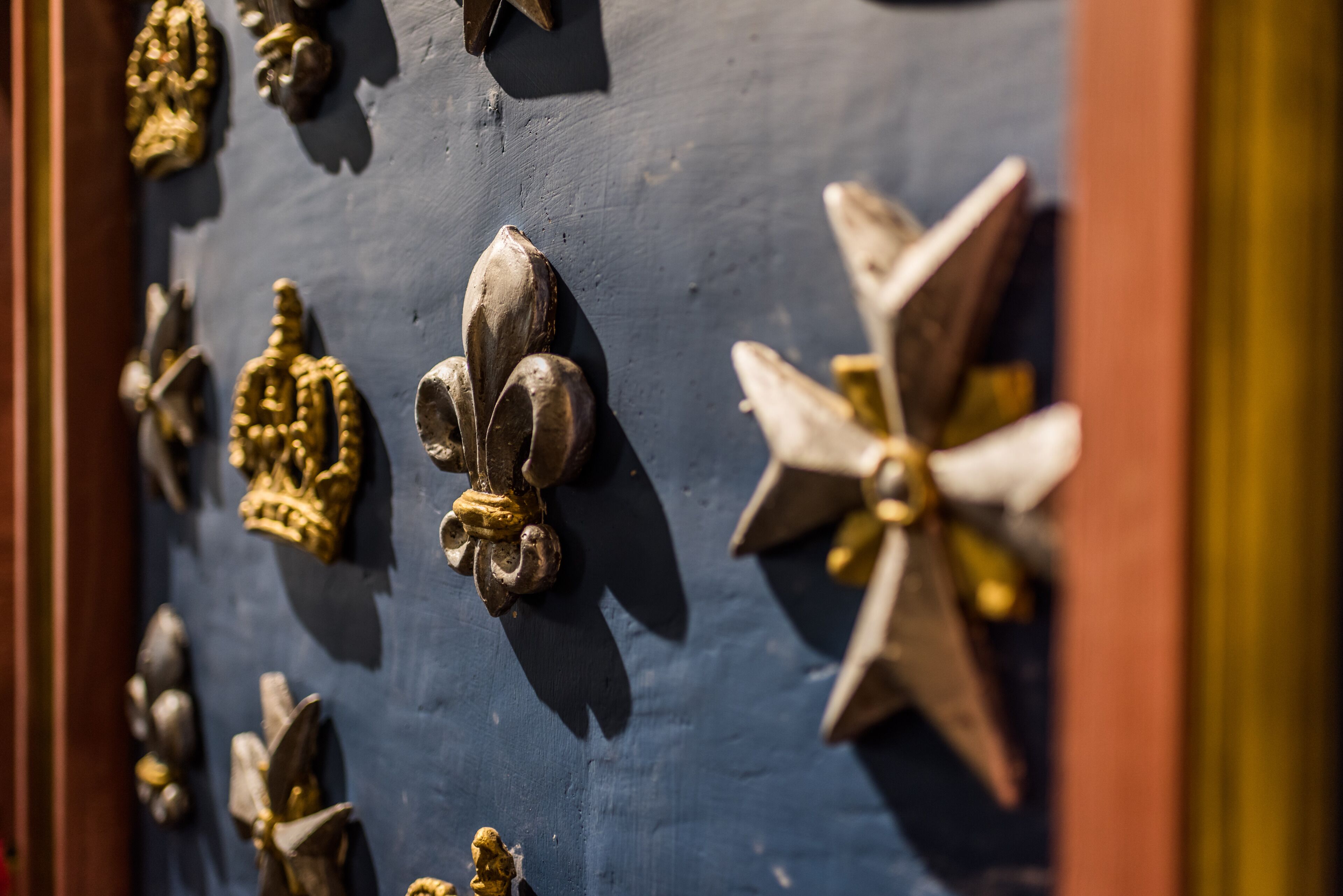 Primer plano de una puerta con diversos adornos de metal y piedra, incluyendo motivos de flores de lis y estrellas.