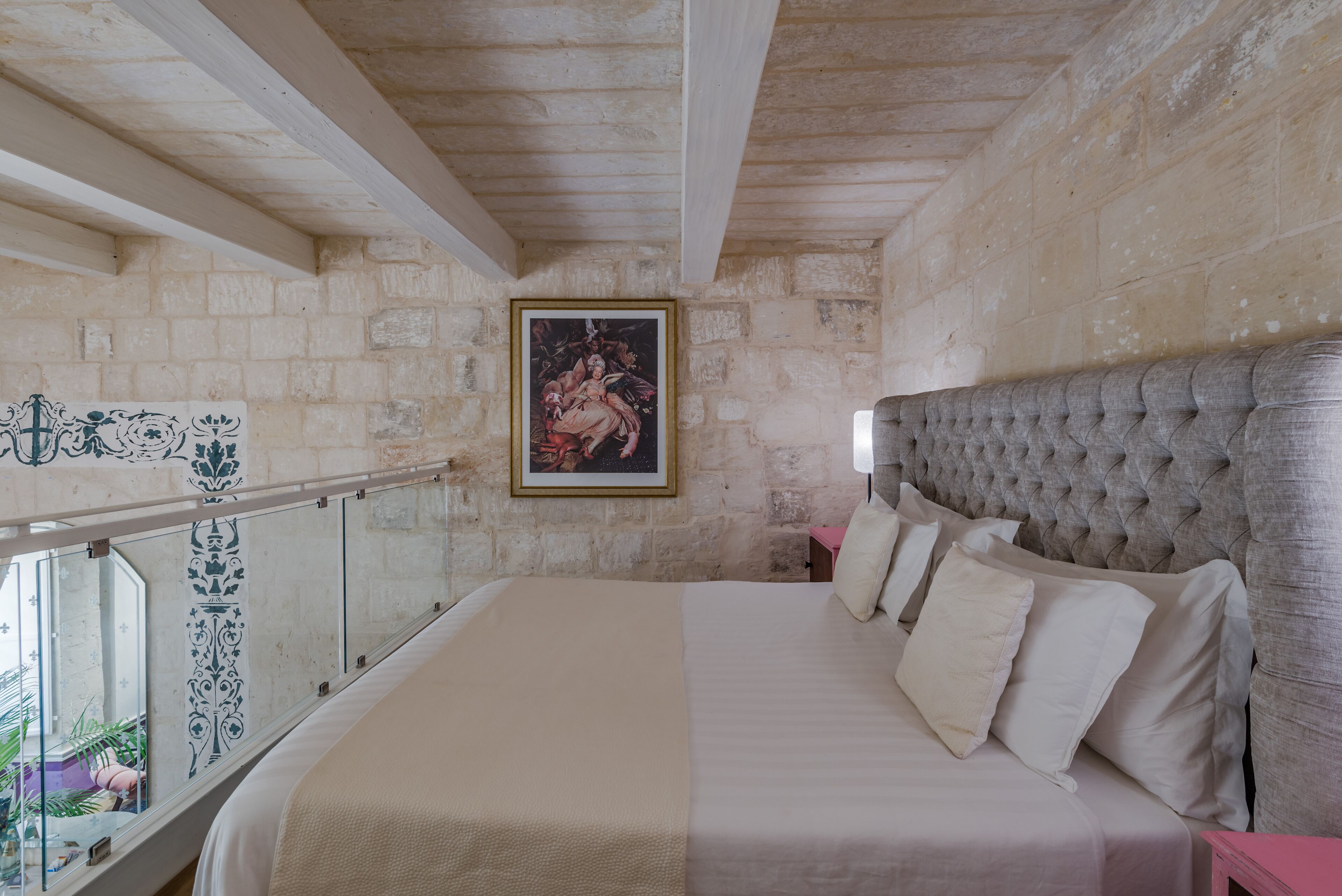 A bedroom with a large bed, a headboard, a framed picture on the wall, and a balcony with a railing.