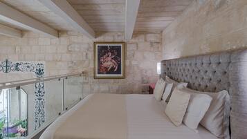 A bedroom with a large bed, a headboard, a framed picture on the wall, and a balcony with a railing.
