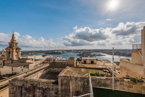 Un paisaje urbano costero con edificios históricos, una destacada torre de iglesia y vistas al mar.