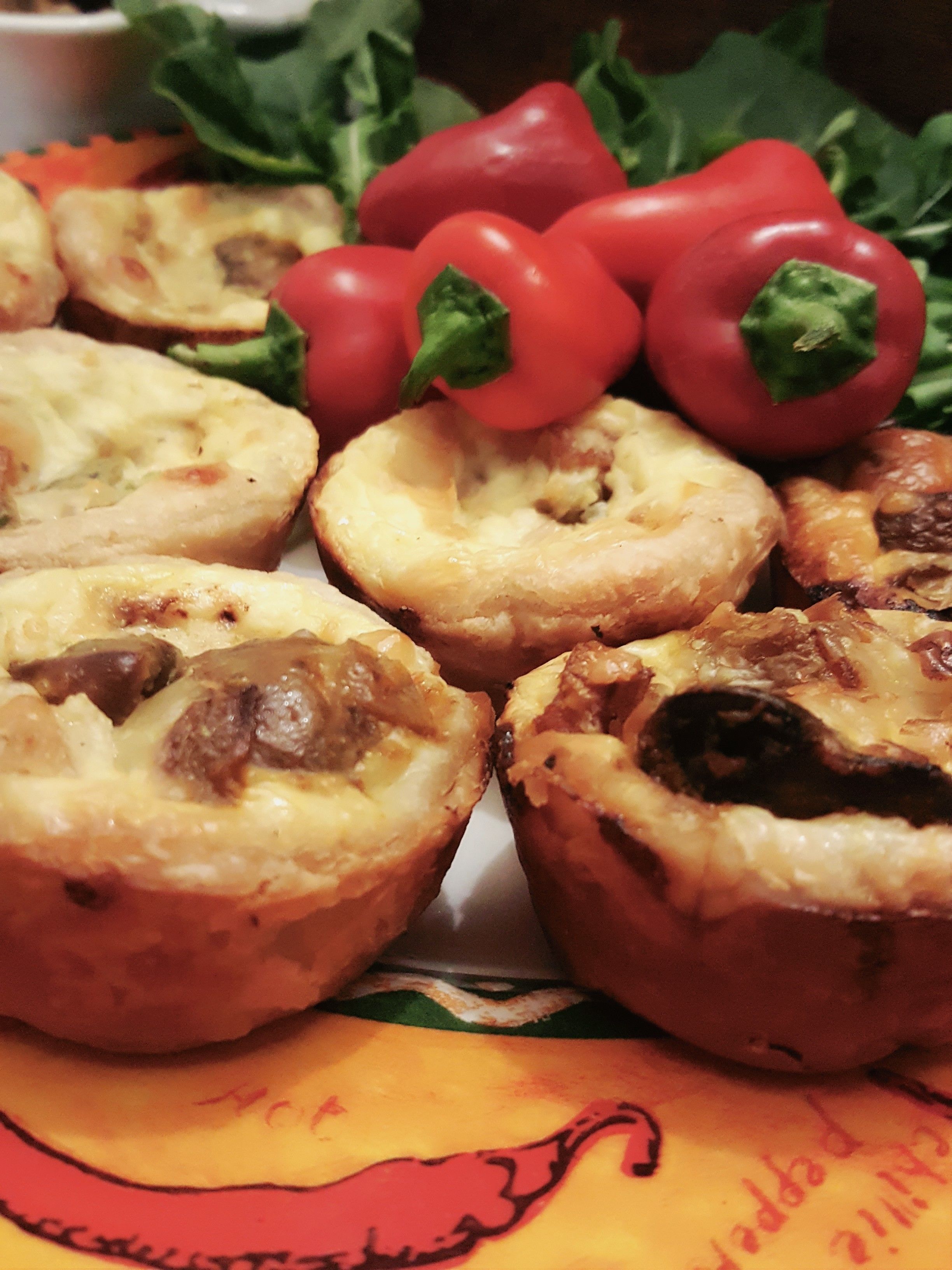 Un plato de mini quiches con champiñones y queso, rodeado de pimientos rojos y lechuga.