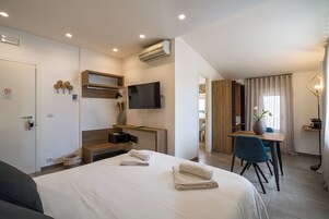 Quarto de hotel moderno com cama, escrivaninha, cadeira, televisão e ar condicionado.