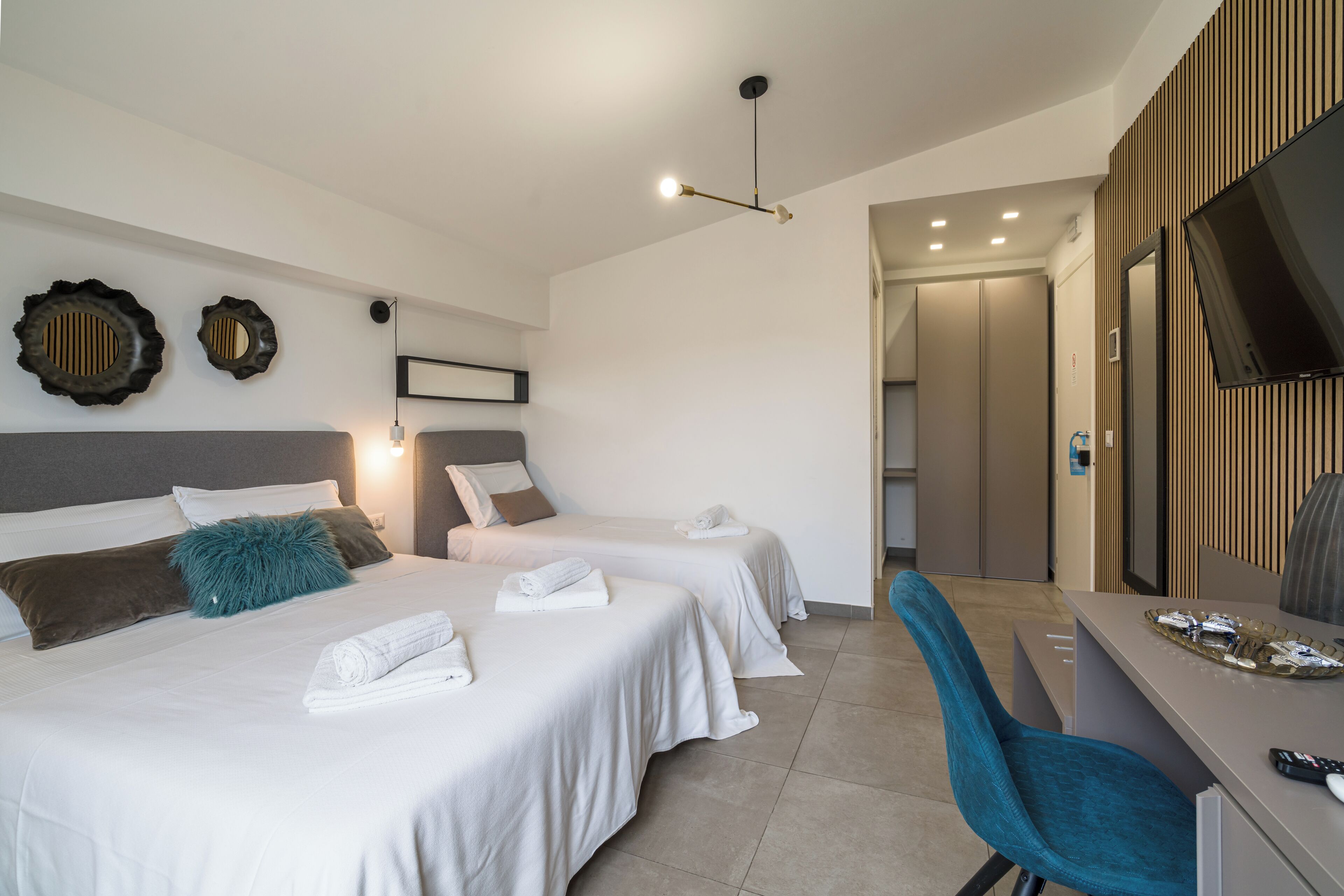 Habitación de hotel con dos camas, un escritorio, un televisor y un baño visible a través de una puerta abierta.