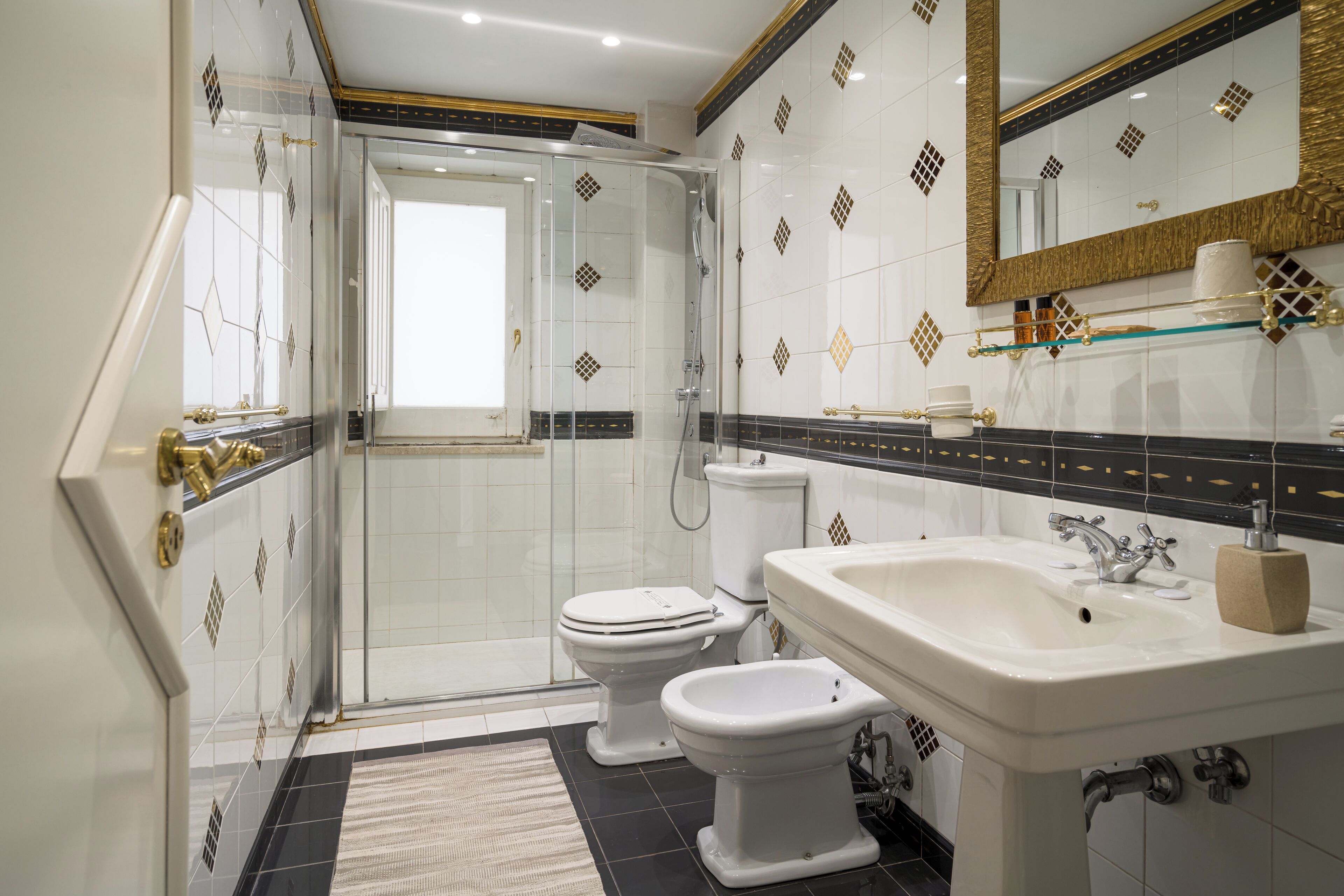 A bathroom with a glass shower enclosure, two toilets, a sink, and a mirror.