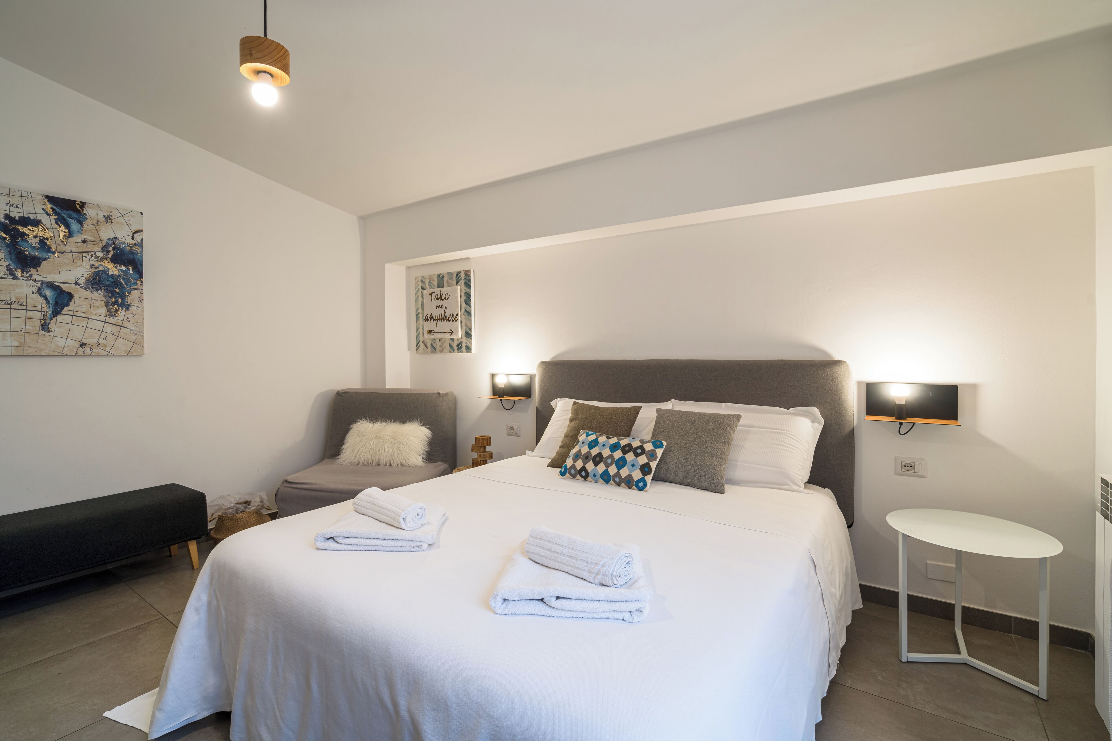 A modern hotel room with a large bed, a chair, a small table, and a map on the wall.