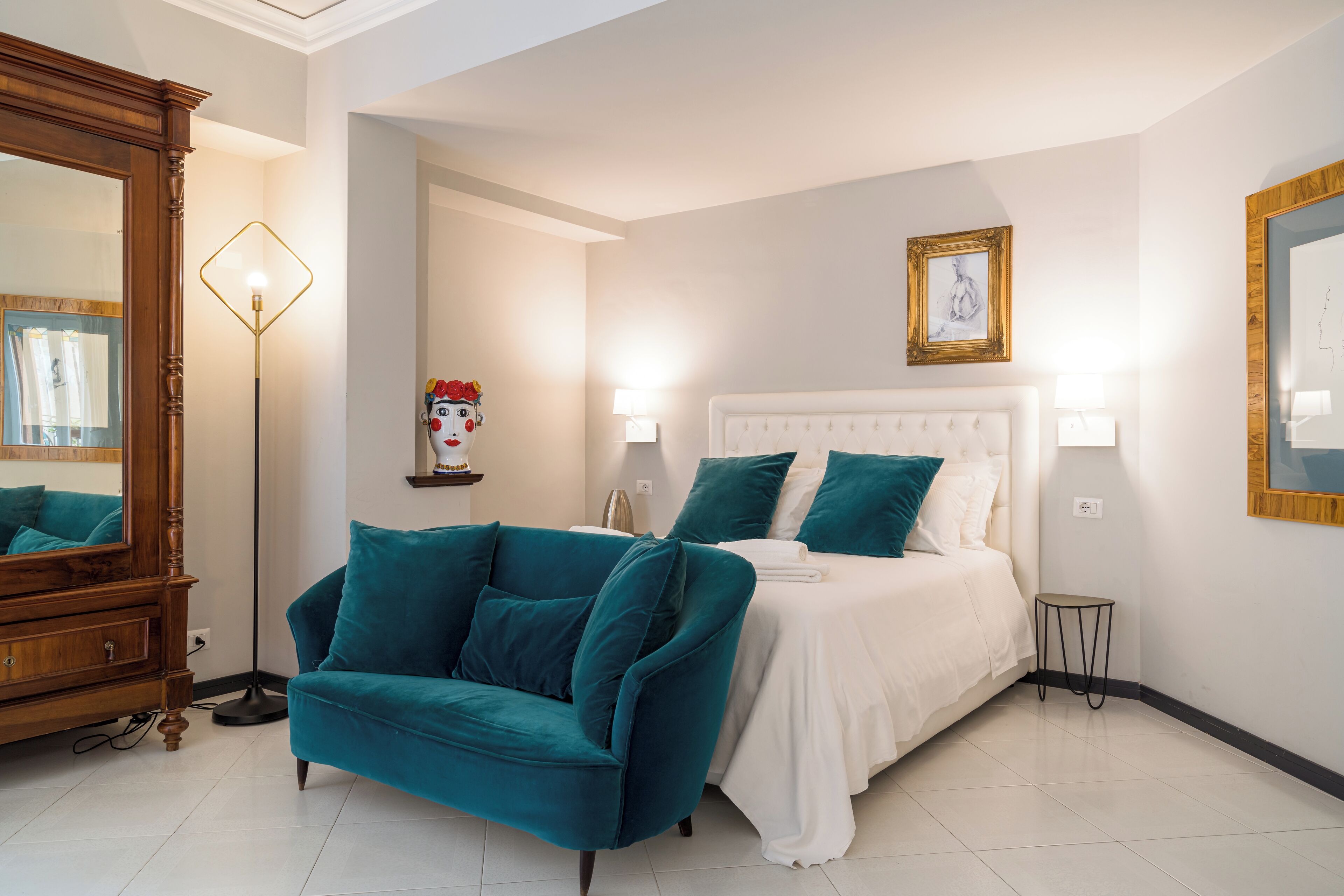 A bedroom with a bed, a teal sofa, a wooden dresser, and a floor lamp.