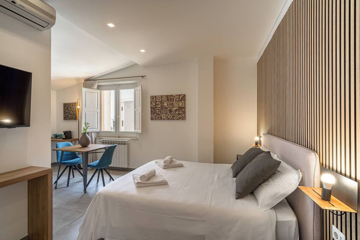 A modern hotel room with a neatly made bed, a desk with a chair, and a large window.