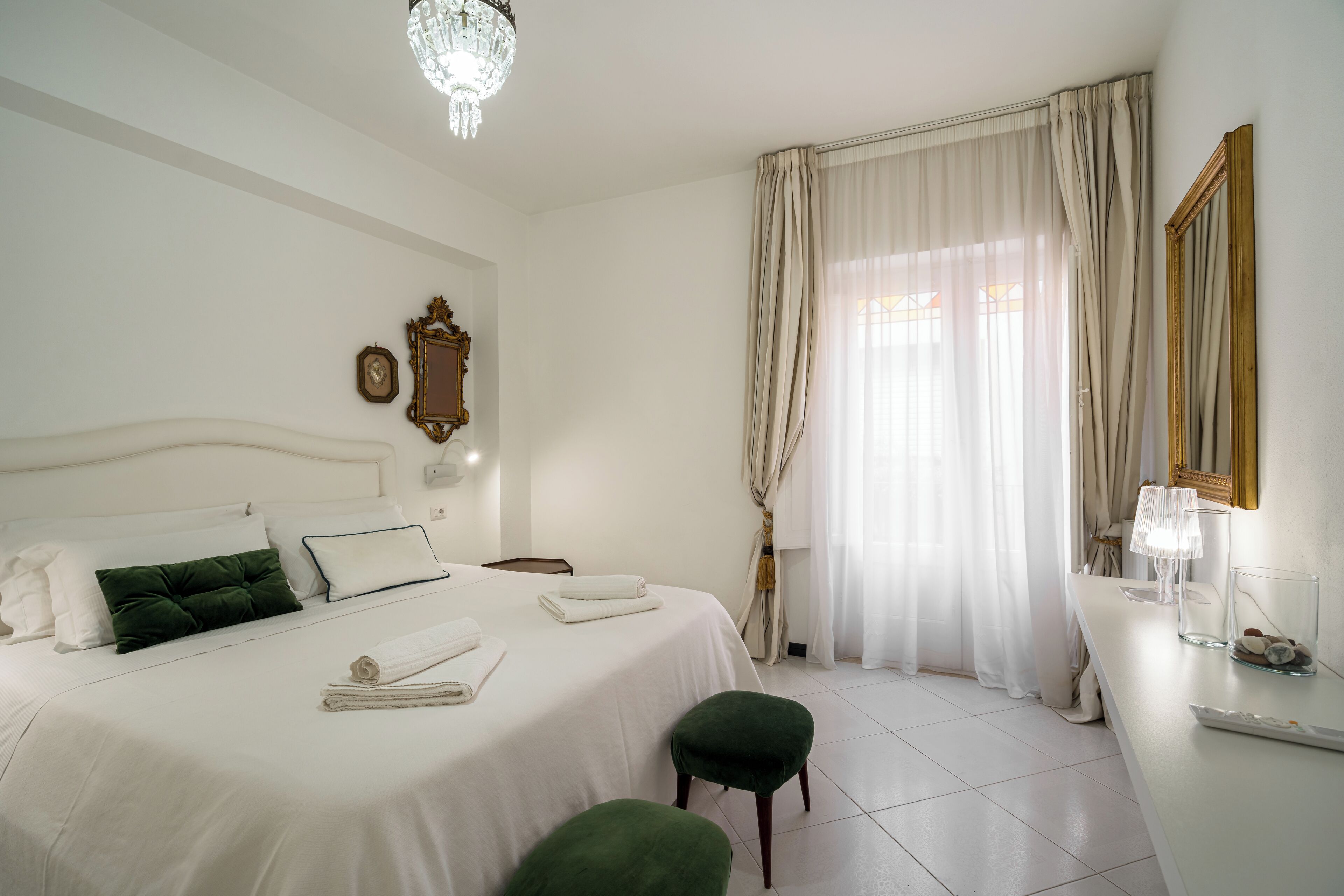 A hotel room with a neatly made bed, a bedside table with a lamp, and a large window with curtains.