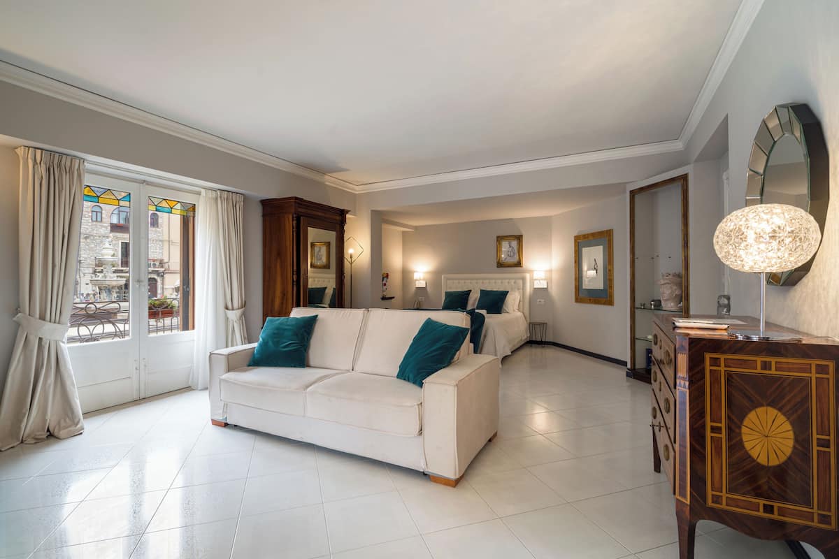 A spacious living room with a white sofa, a wooden cabinet, and a large mirror.