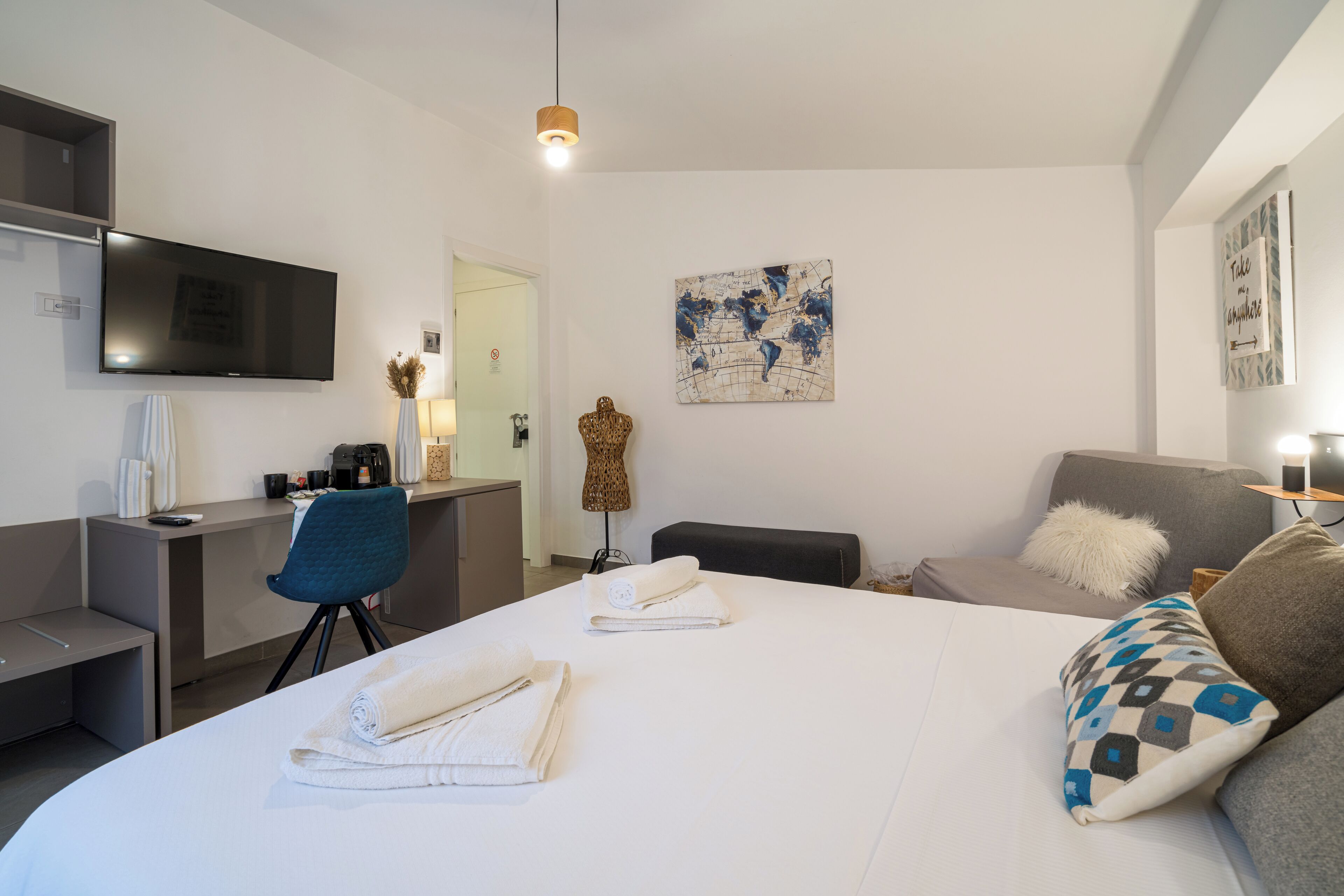 A modern hotel room with a large bed, a desk with a flat-screen TV, a sofa, and a decorative wall piece.