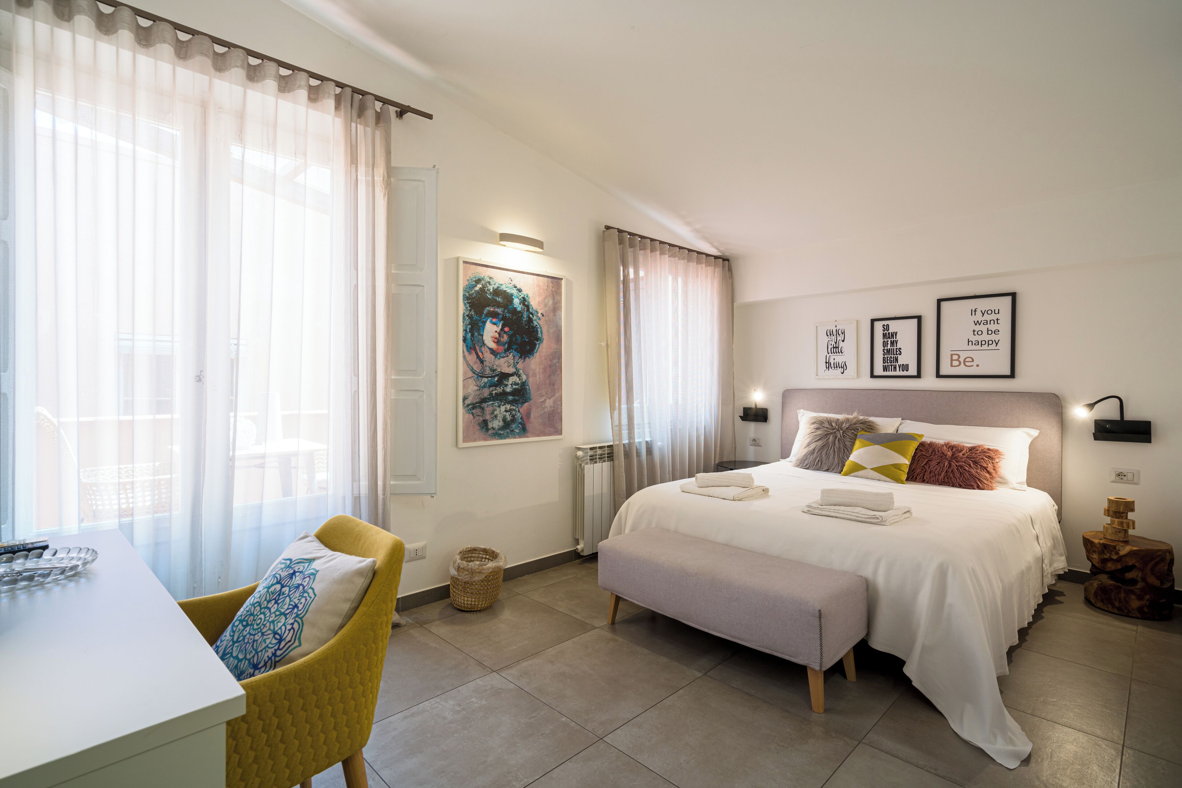 A hotel room with a bed, bedside table, chair, and artwork on the walls.