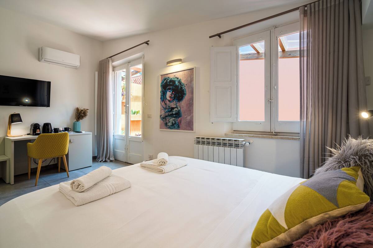 A hotel room with a bed, a desk, a chair, a TV, and a painting on the wall.