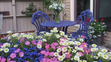 A patio with a round table and two chairs, surrounded by a variety of colorful flowers.