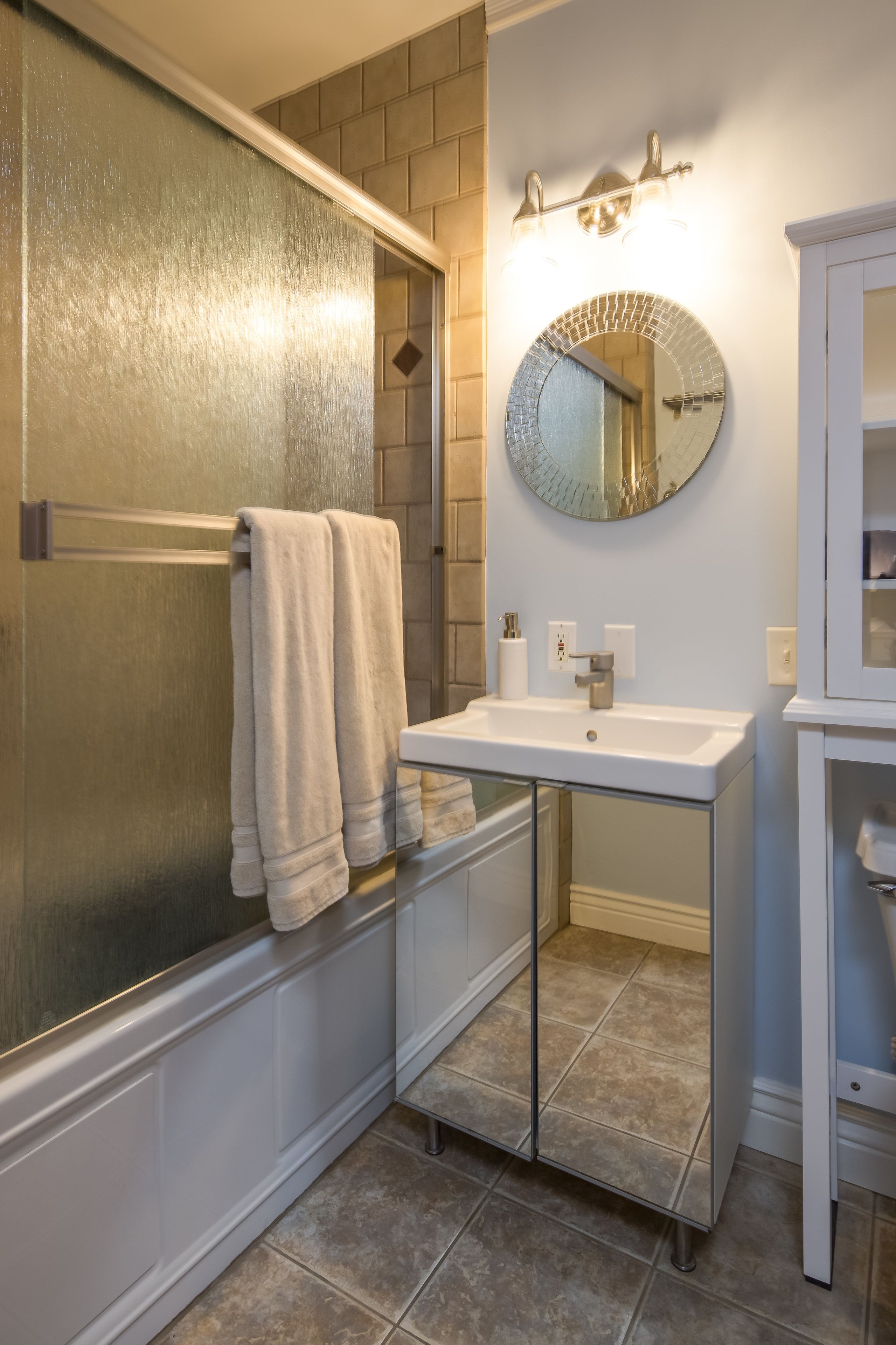 A bathroom with a glass shower enclosure, a sink with a mirror above it, and a towel rack.