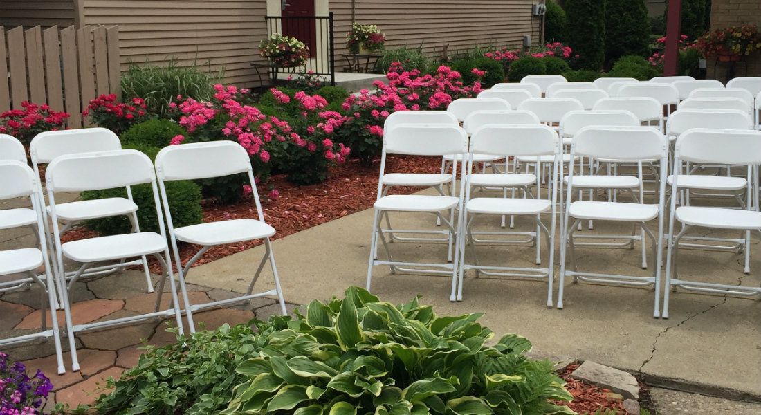 Des tables et des chaises disposées en rangées à l’extérieur, avec un jardin en arrière-plan.