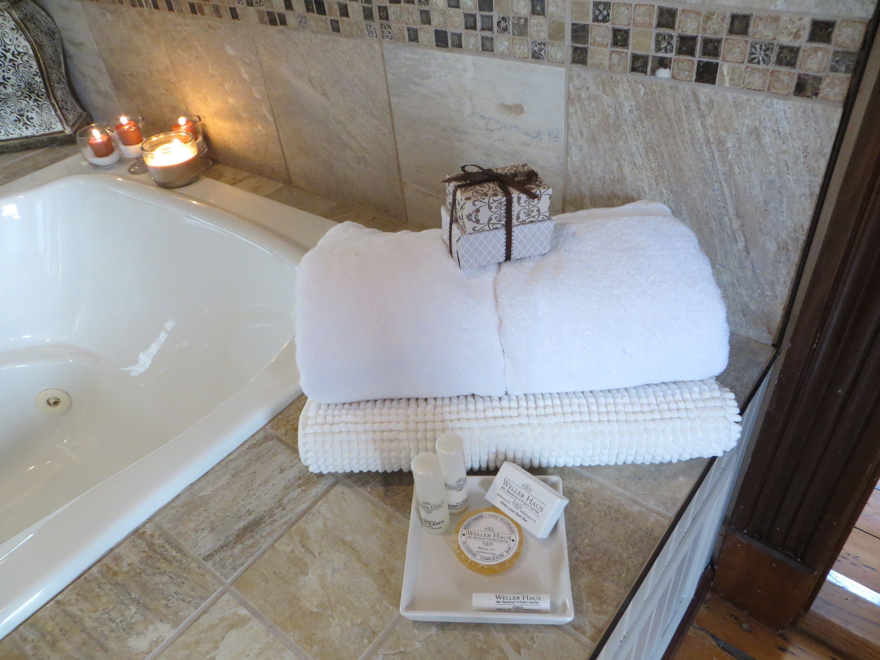 A bathroom with a bathtub, candles, towels, and toiletries.