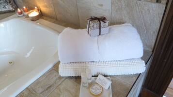 A bathroom with a bathtub, candles, towels, and toiletries.