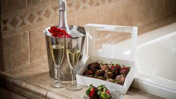Una botella de champán, dos copas y una caja de fresas cubiertas de chocolate sobre una encimera de baño.
