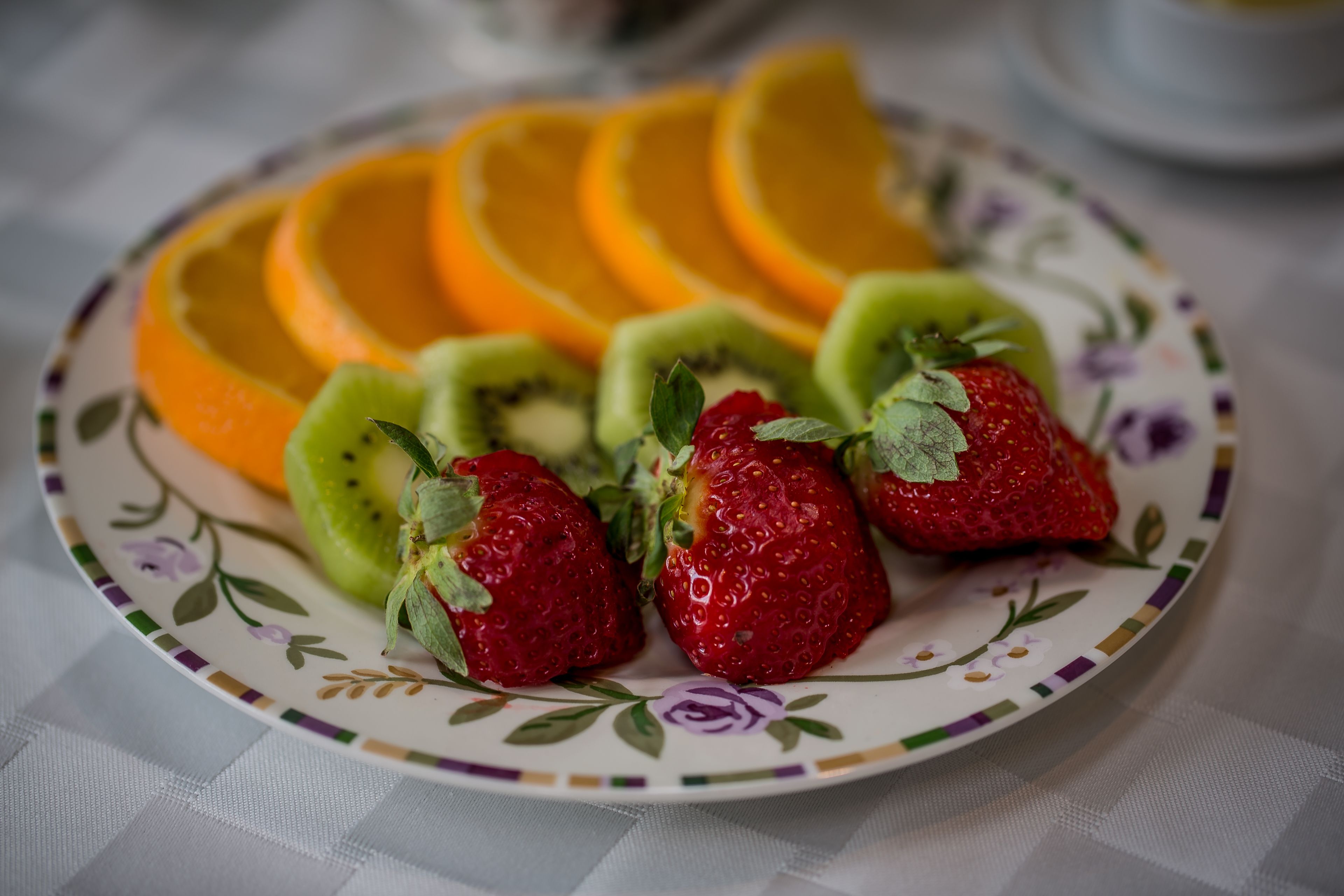 Un plato con rodajas de naranja, kiwi y fresas, sobre un plato estampado con motivos florales.