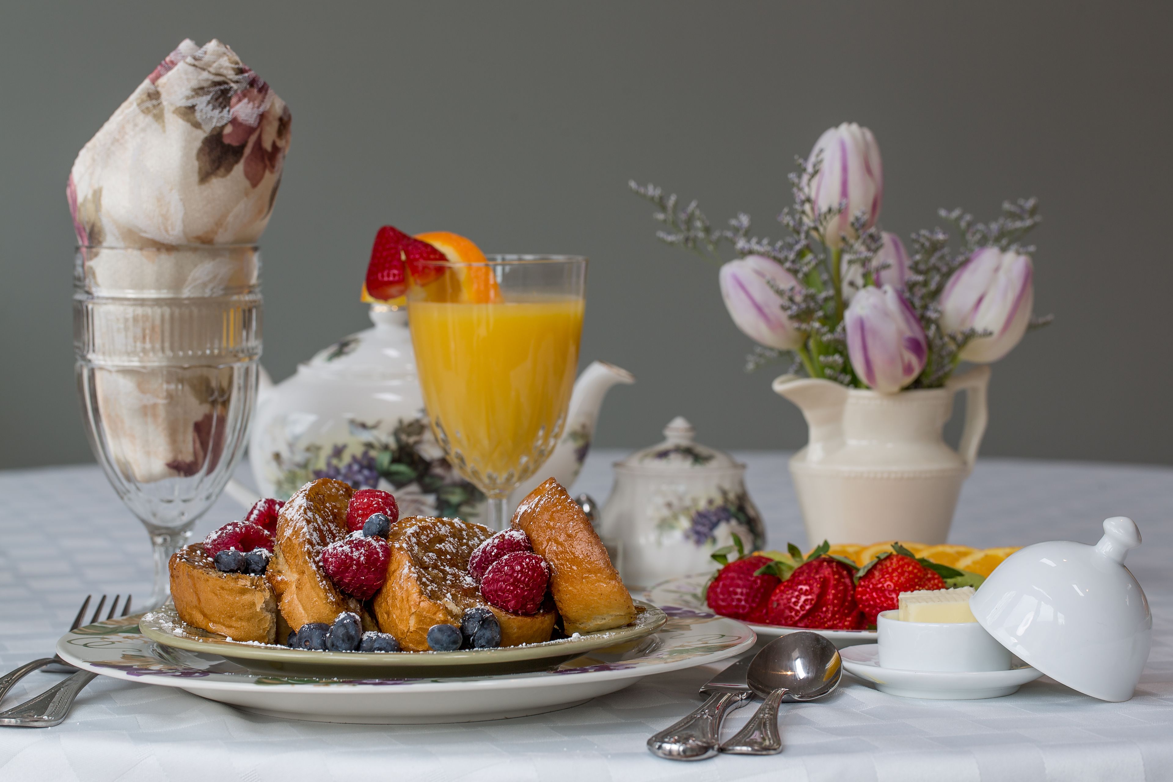 A breakfast setting with waffles, berries, a glass of orange juice, and a teapot.