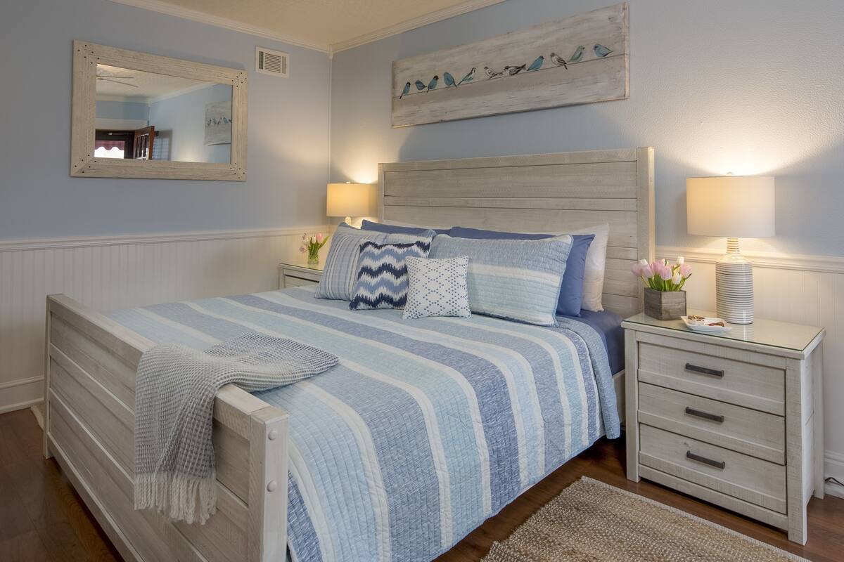 A bedroom with a bed, bedside tables, a mirror, and wall art.