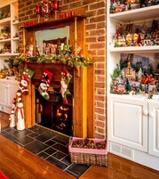 A fireplace with a brick mantle, surrounded by Christmas decorations including stockings, a garland, and a small Christmas village display.