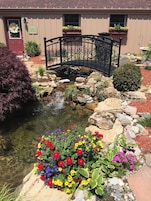 An outdoor garden with a small pond, colorful flowers, a bridge, and a building labeled "EVENT CENTER".