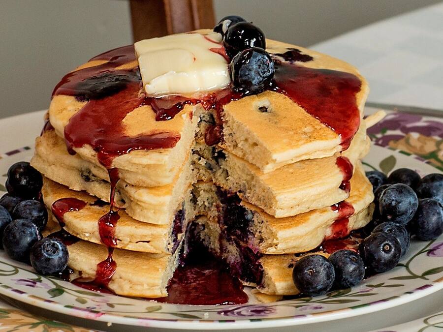 A stack of pancakes with blueberries and syrup on a floral plate.