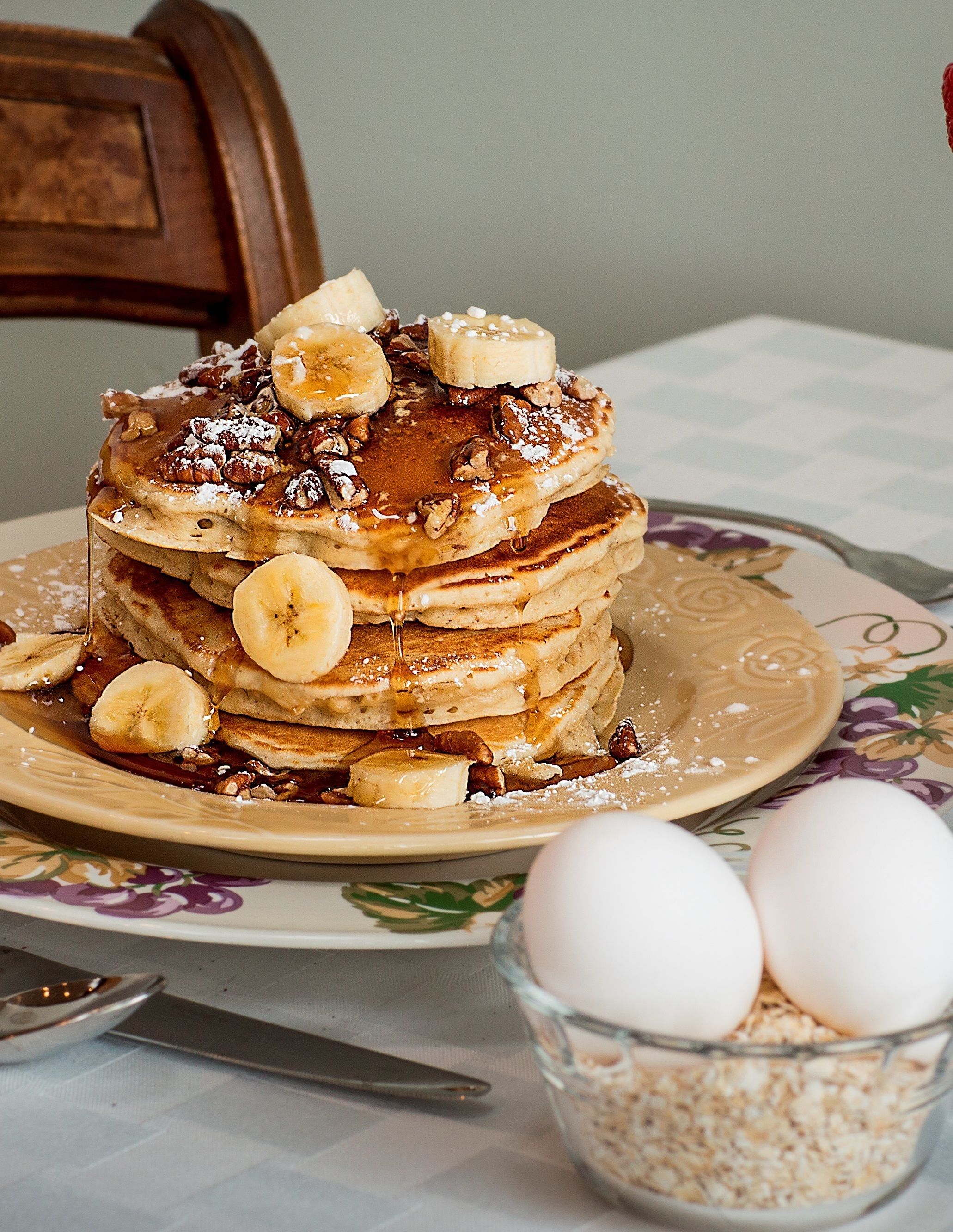 A stack of pancakes with bananas and syrup on a floral plate.