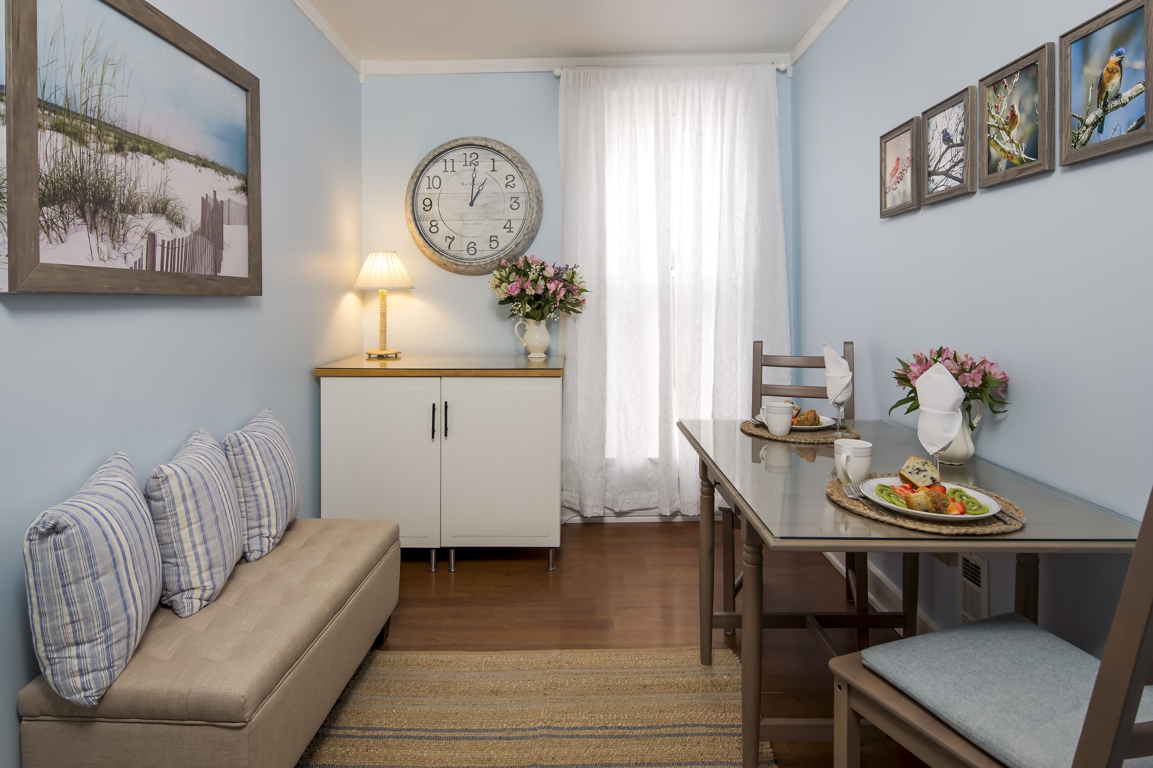 A cozy room with a sofa, a dining table with a plate of food, a clock, and a vase of flowers.