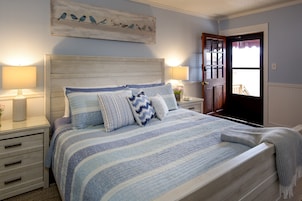 A bedroom with a bed, two bedside tables, a nightstand, a door, and a wall-mounted artwork.