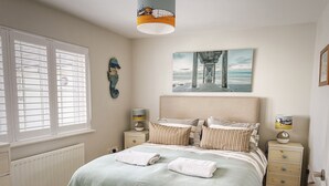 Een slaapkamer met een bed, twee nachtkastjes, een radiator, een raam met zonwering en een kunstwerk aan de muur.