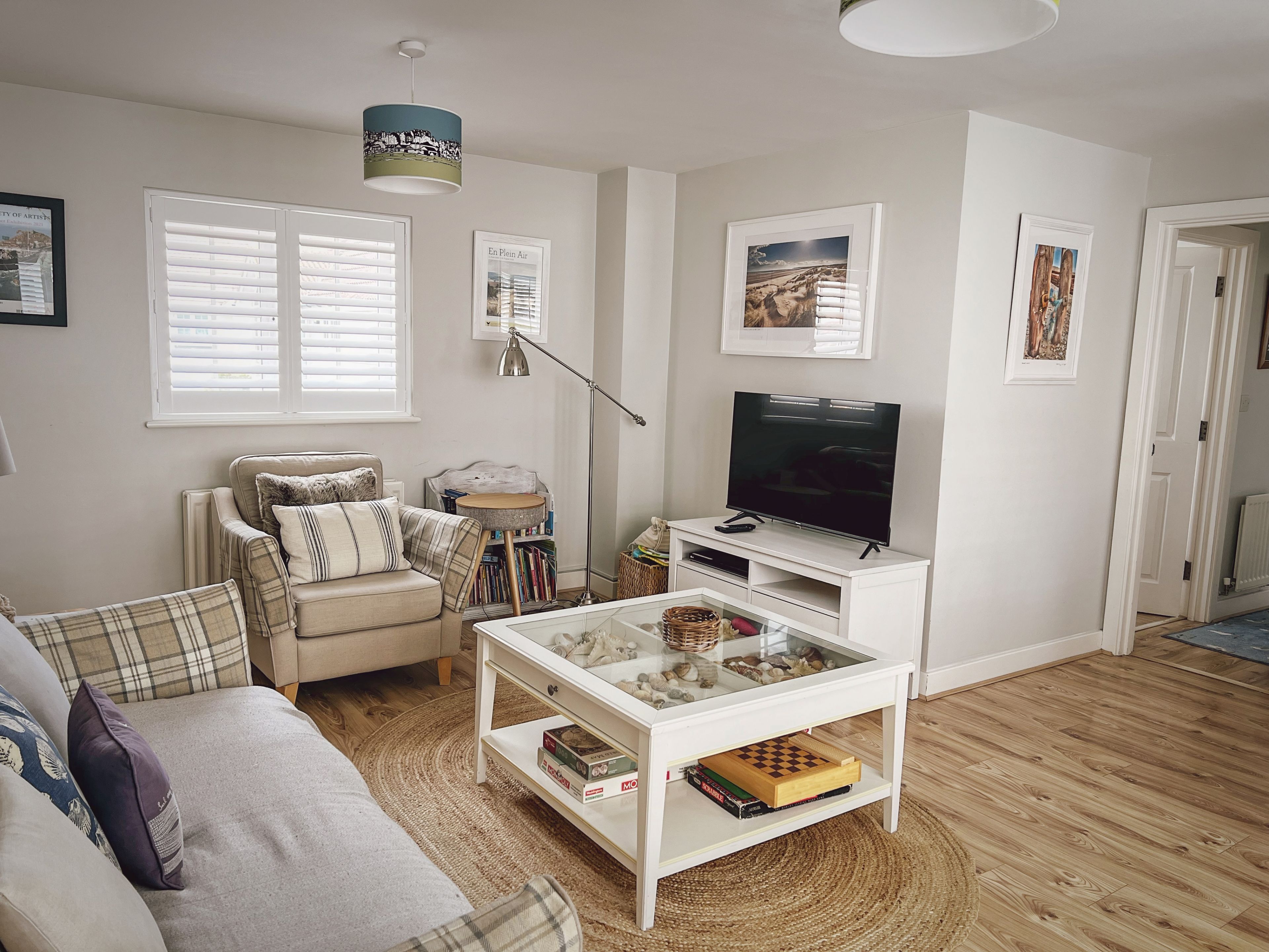 Een woonkamer met een bank, fauteuil, salontafel, televisie en kunstwerken aan de muur.