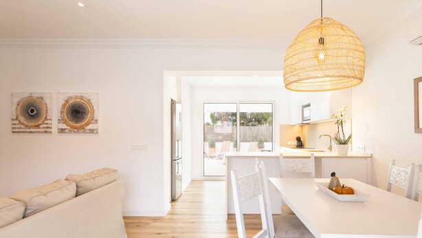 Een moderne keuken met witte kasten, een eettafel en een hangende lamp.