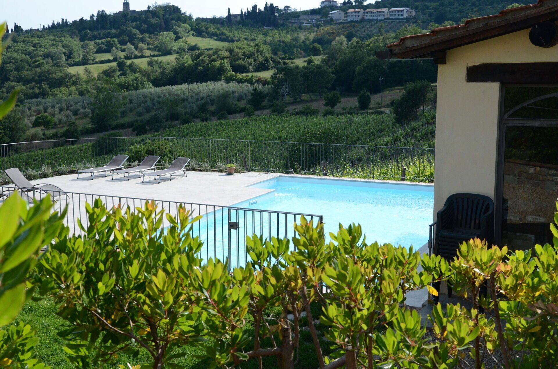 Piscina con sillas de descanso, rodeada de vegetación y vistas a colinas.