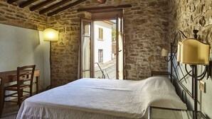A rustic room with a stone wall, a wooden bed with a white bedspread, a wooden chair, and a table. - Nice apartment for 2 people with WIFI, pool, TV and pets allowed, close to Arezzo (Capolona)