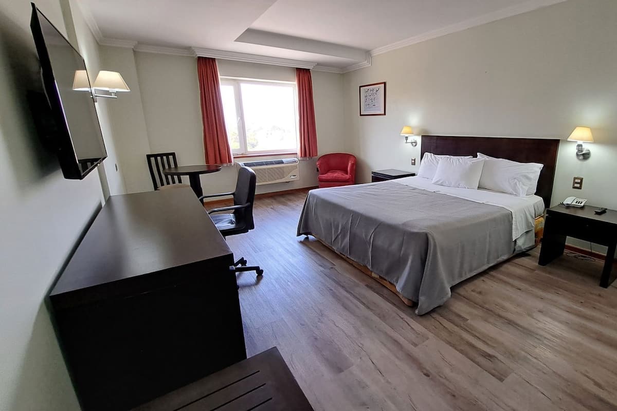Hotellihuone, jossa on sänky, yöpöydät, työpöytä, tuoli, televisio ja ikkuna, jossa on verhot.