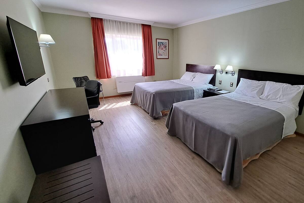 Hotellihuone, jossa on kaksi sänkyä, työpöytä, tuoli, televisio ja ikkuna, jossa on verhot.