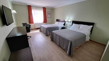 A hotel room with two beds, a desk, a chair, a TV, and a window with curtains.