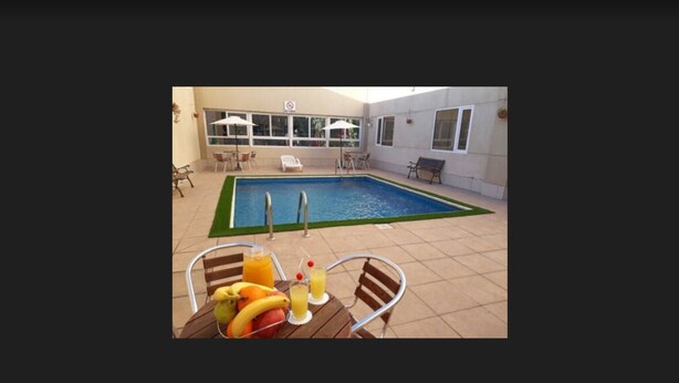 Un área de piscina interior con una mesa dispuesta con fruta y bebidas, rodeada de sillas y sombrillas.