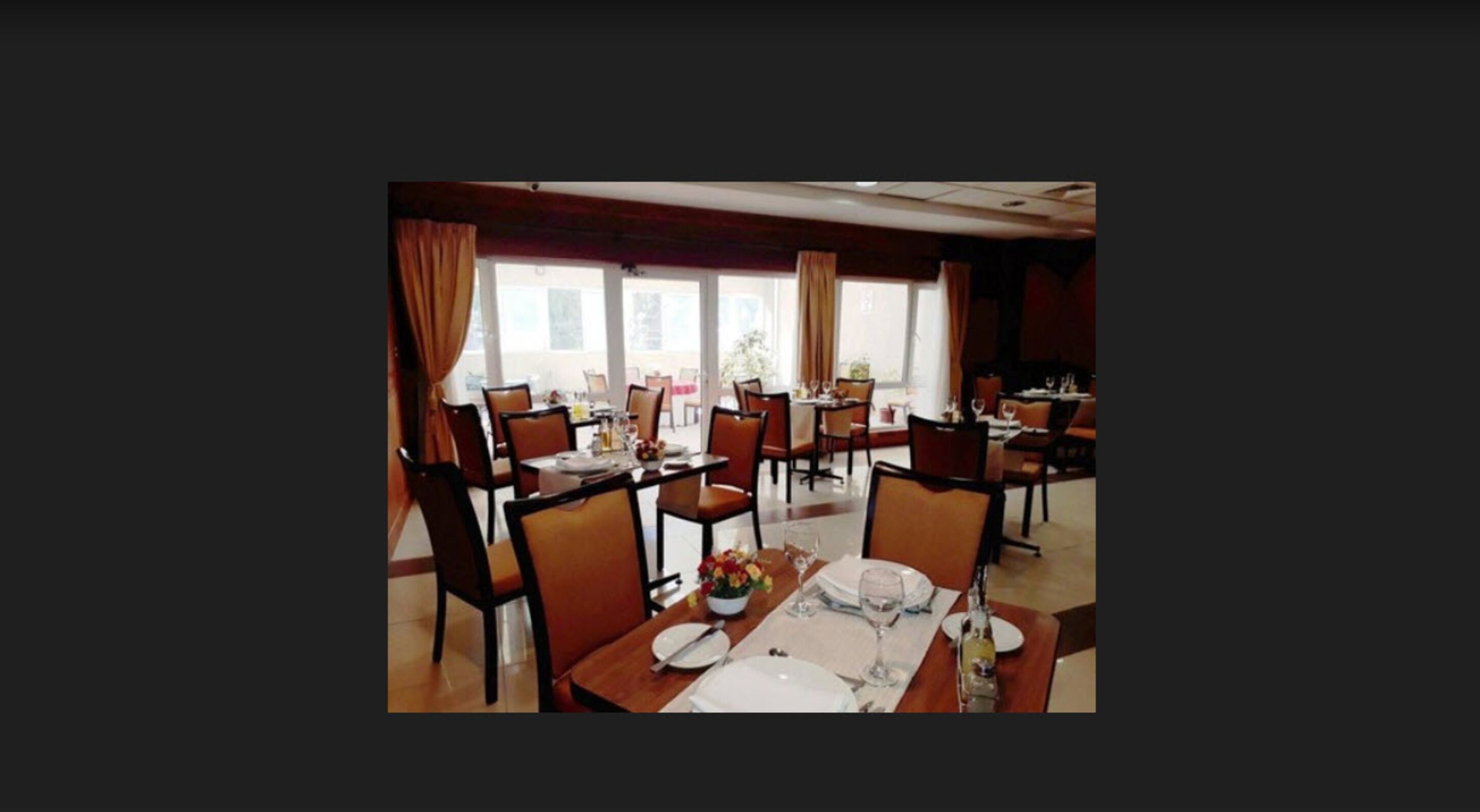 Comedor con mesas dispuestas para el servicio, ventanas amplias y cortinas.